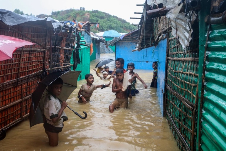 Rohingya refugee children play in flood waters at the Rohingya refugee camp in Kutupalong, Bangladesh in July. [Shafiqur Rahman/File: AP Photo]