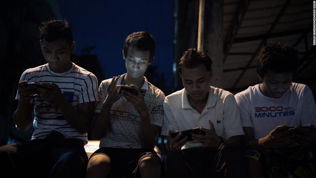 Young men browse Facebook on their smartphones as they sit in a street in Yangon.